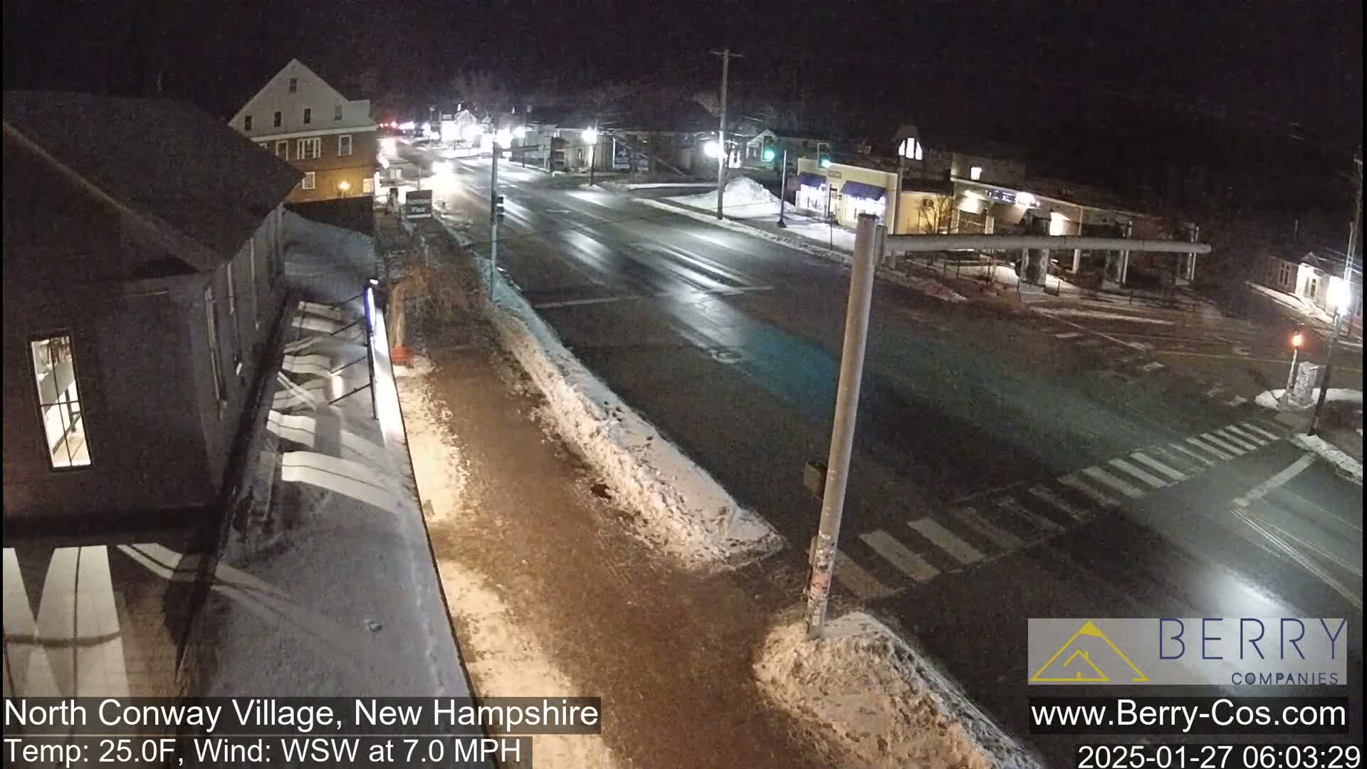 A nighttime street scene shows a mostly empty road with some snow on the sides, under a clear, dark sky.