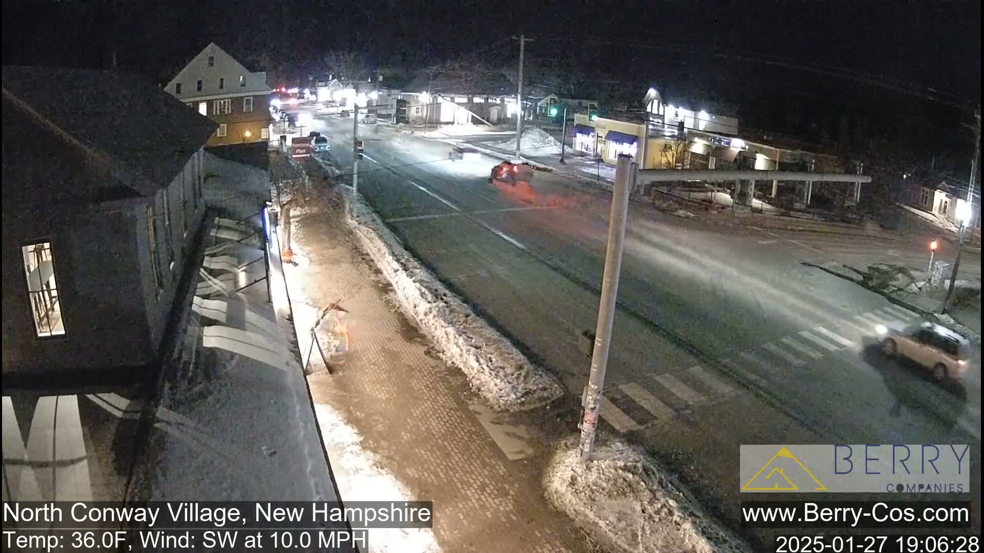 A nighttime street scene shows a lightly snow-covered road with a few cars, some buildings, and a person walking along the sidewalk under a southwest wind of 10 mph, with a temperature of 36°F.