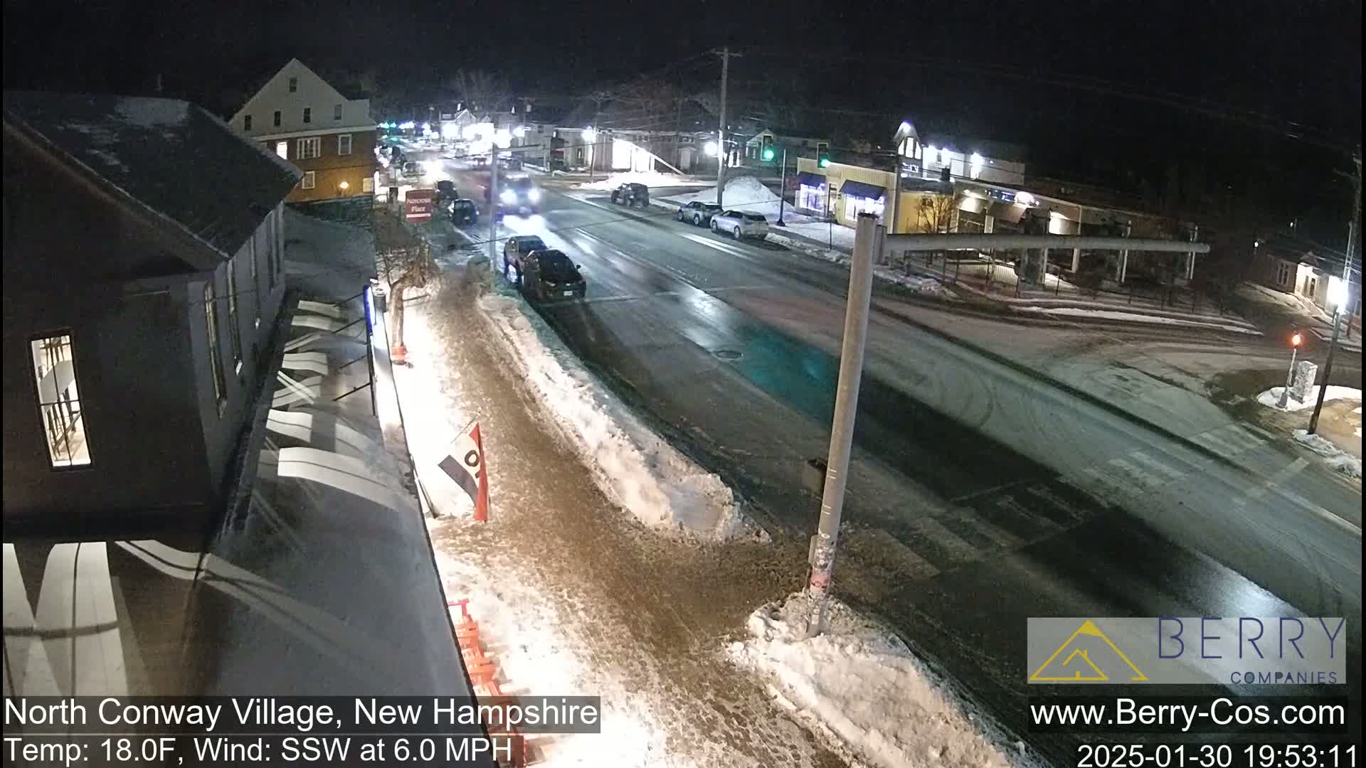 A nighttime street scene shows a partly snow-covered road with several cars and buildings under a dark sky, with a 18°F temperature and a 6.0 mph south-southwesterly wind.