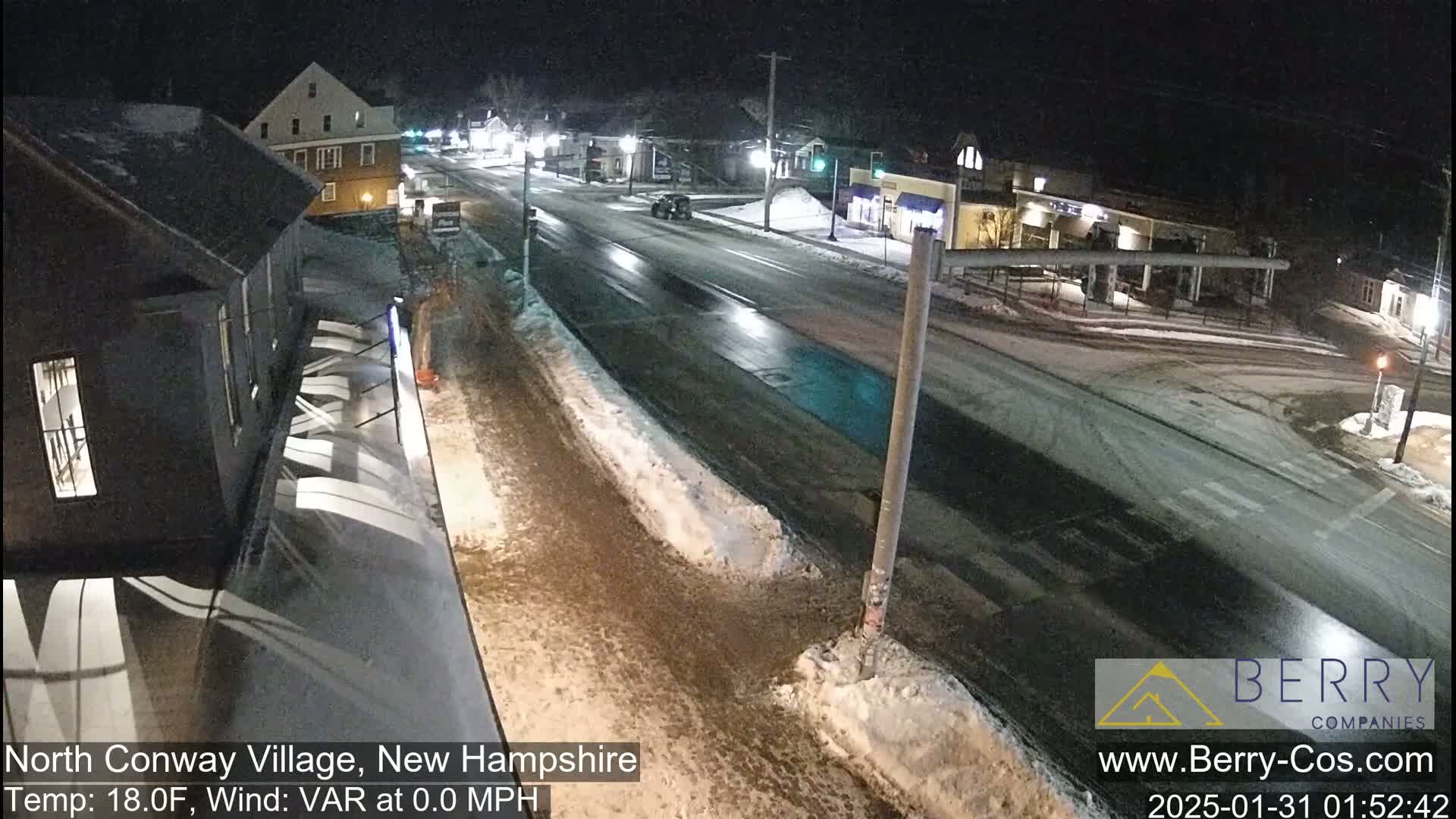 A nighttime view of a snow-covered street in a town with several buildings, under a clear sky.