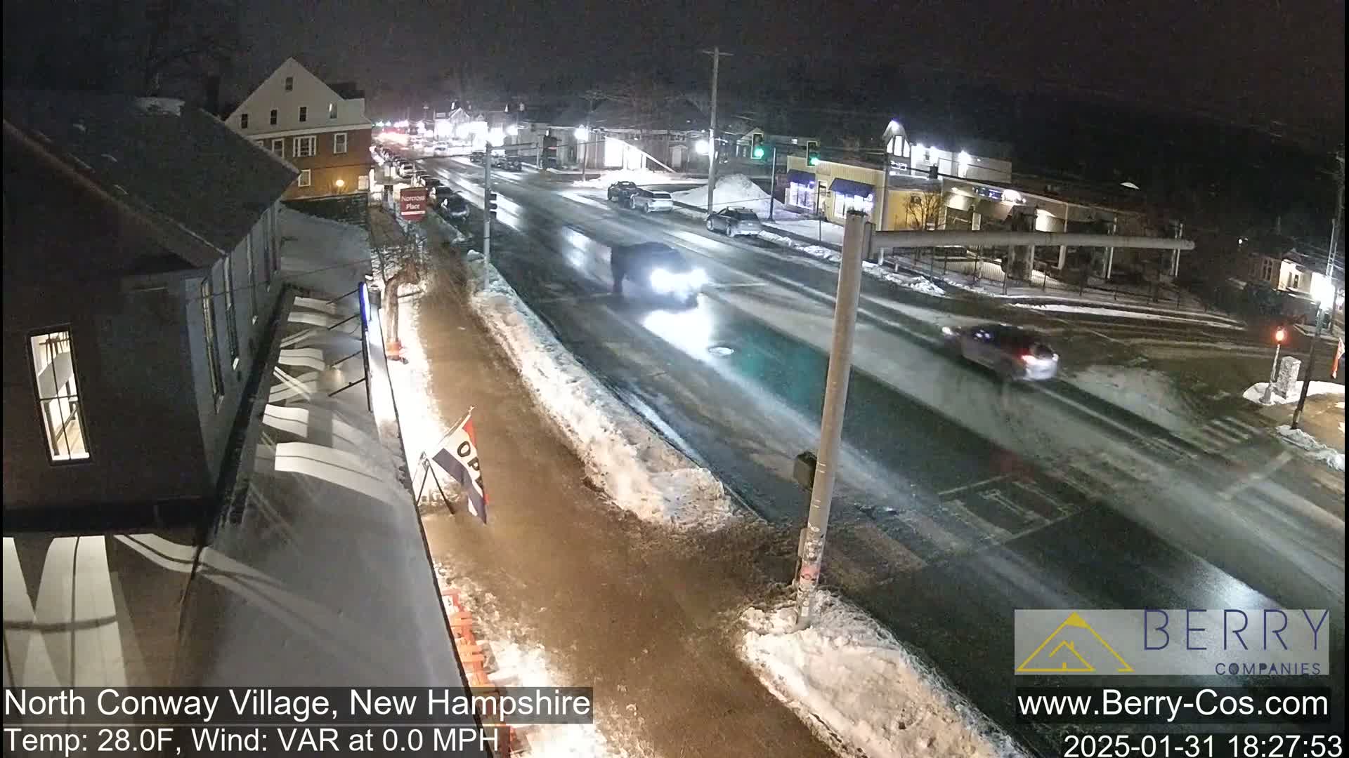 A nighttime street scene shows cars driving on a wet road with patches of snow and ice on the sidewalks.