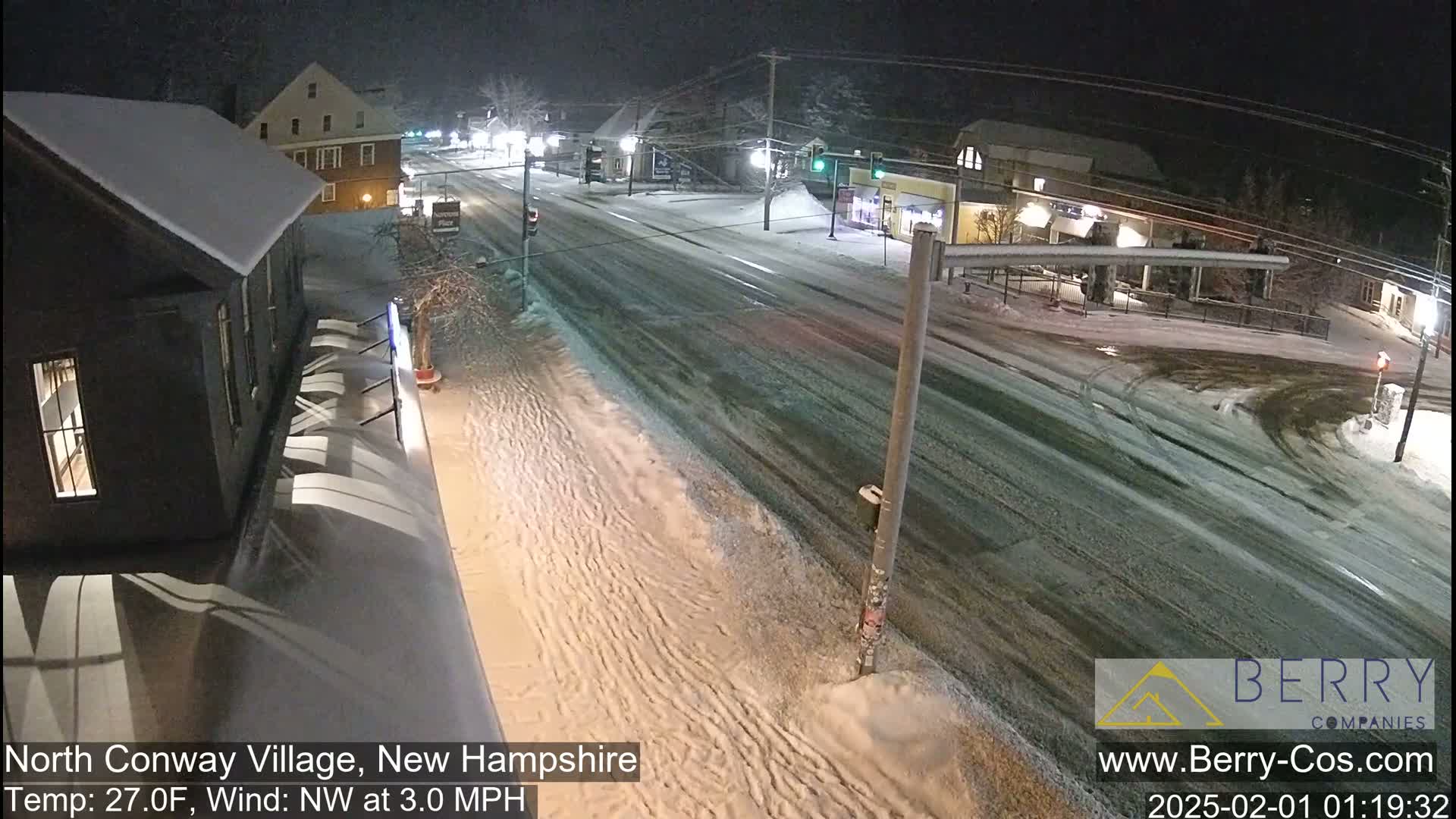 A snow-covered street scene at night, with buildings and sparsely traveled roads.