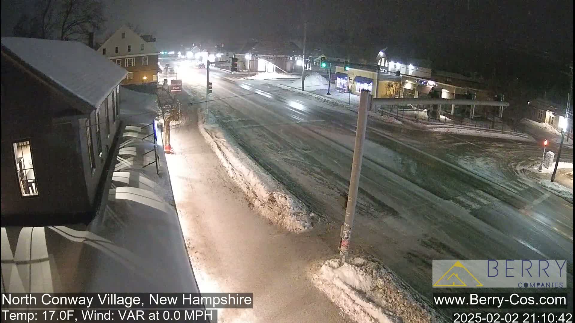 A snow-covered street scene at night shows a sparsely traveled road and several buildings under low light conditions.