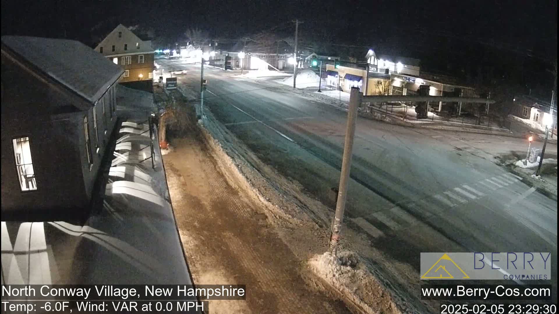 A nighttime street scene shows a snow-covered road and buildings under a clear sky, with a temperature of -6°F and no wind.