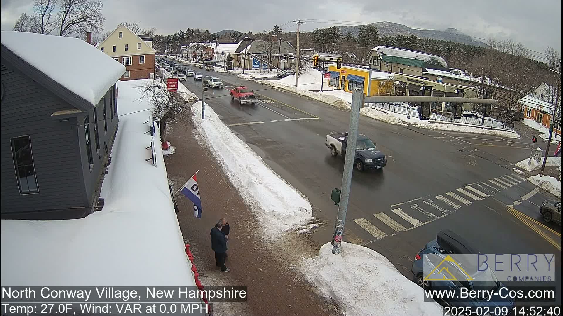 A snow-covered street scene shows several vehicles at an intersection under an overcast sky.