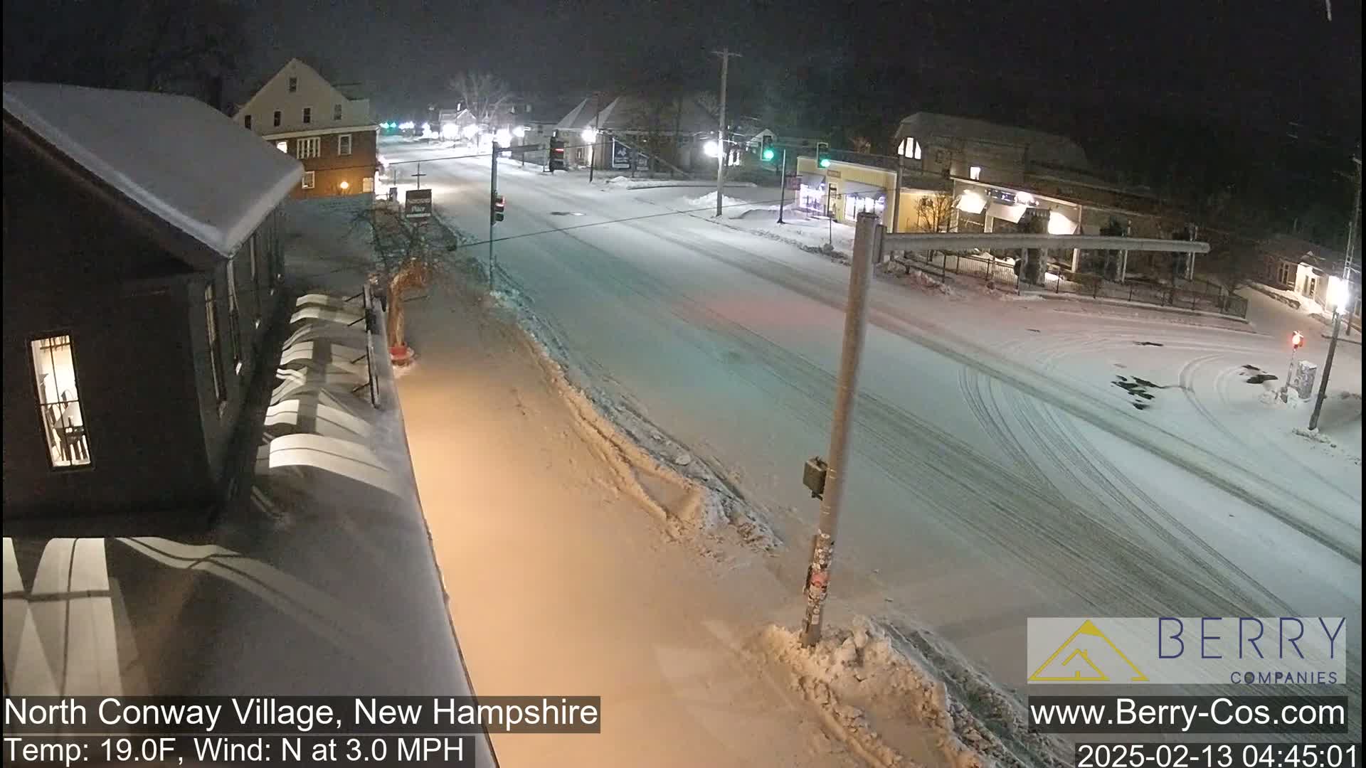 A snow-covered street scene at night, with buildings and a few cars visible under a dark sky.