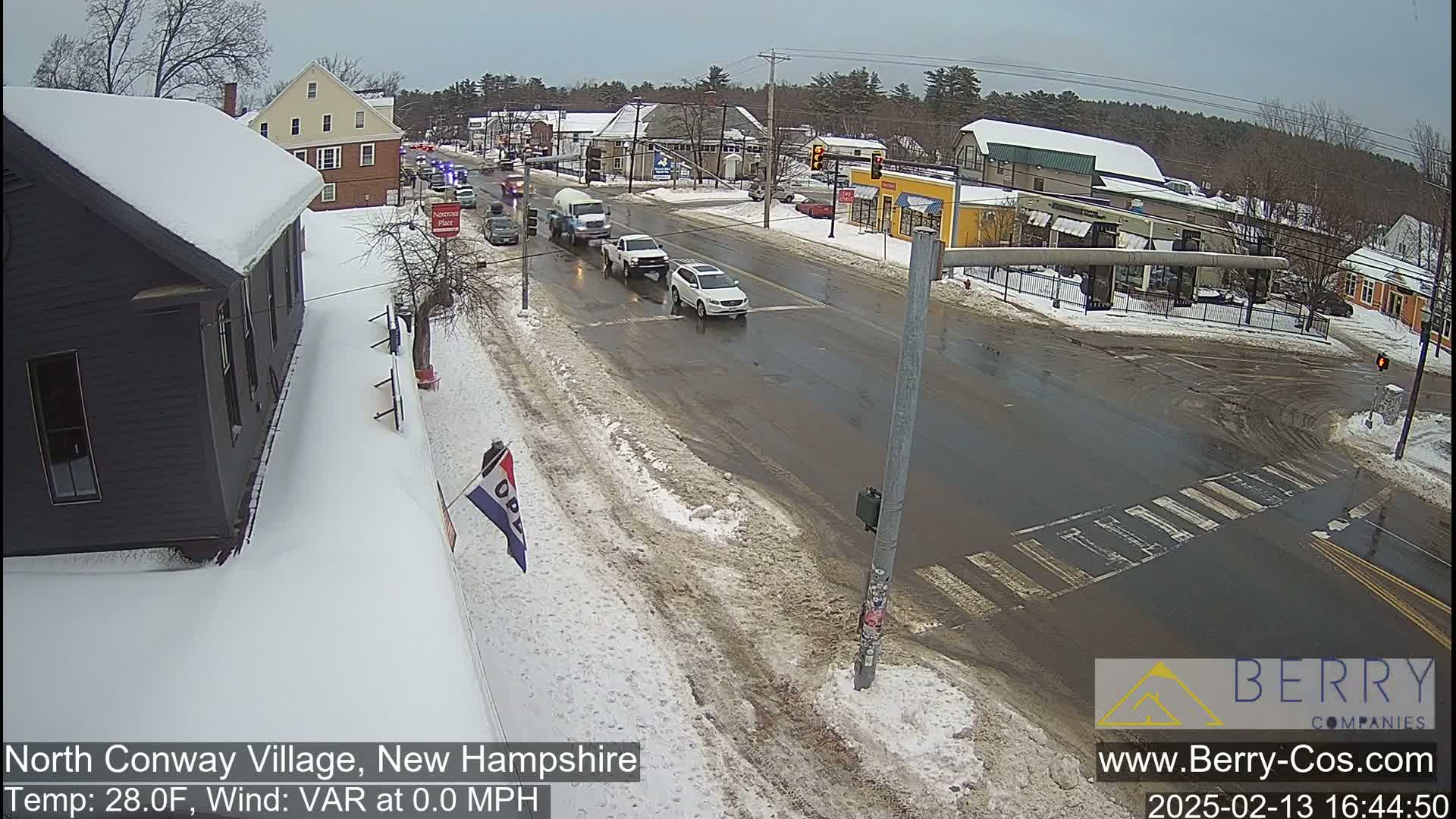 A snow-covered street scene shows several vehicles at a slushy intersection on a cloudy day.