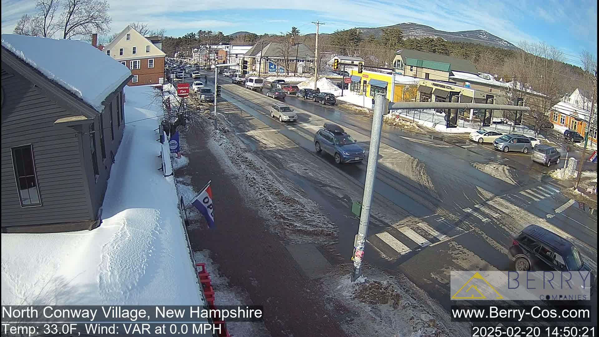 A snow-covered street scene in a small town shows several vehicles at an intersection on a sunny, cold day.