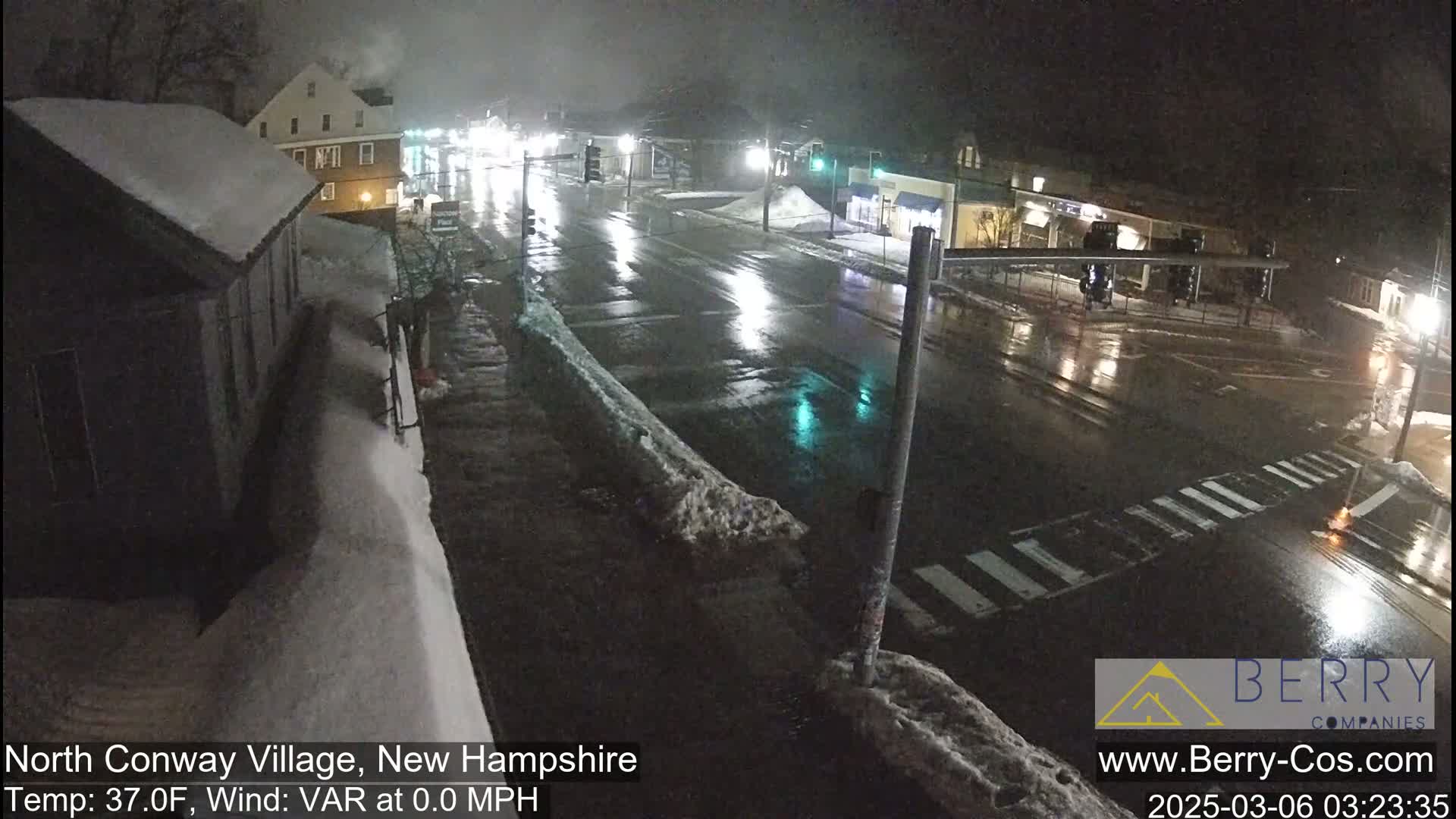A wet, nighttime street scene shows a snow-covered roadway and buildings under a dark sky.