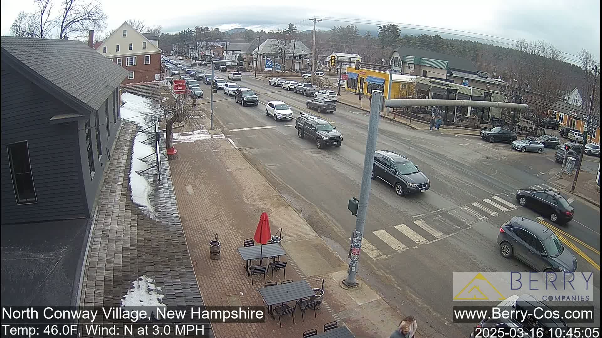 A street scene shows cars driving on a road that intersects with another road, with some snow and ice patches on the ground under an overcast sky.