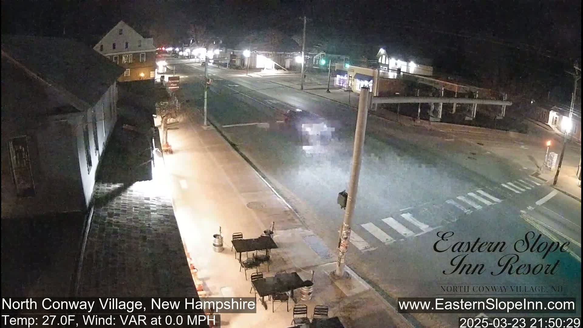 A nighttime street scene shows a mostly empty road with a vehicle in the distance, outdoor seating at a business, and buildings along the sides of the street under calm, clear conditions with a temperature of 27 degrees Fahrenheit.