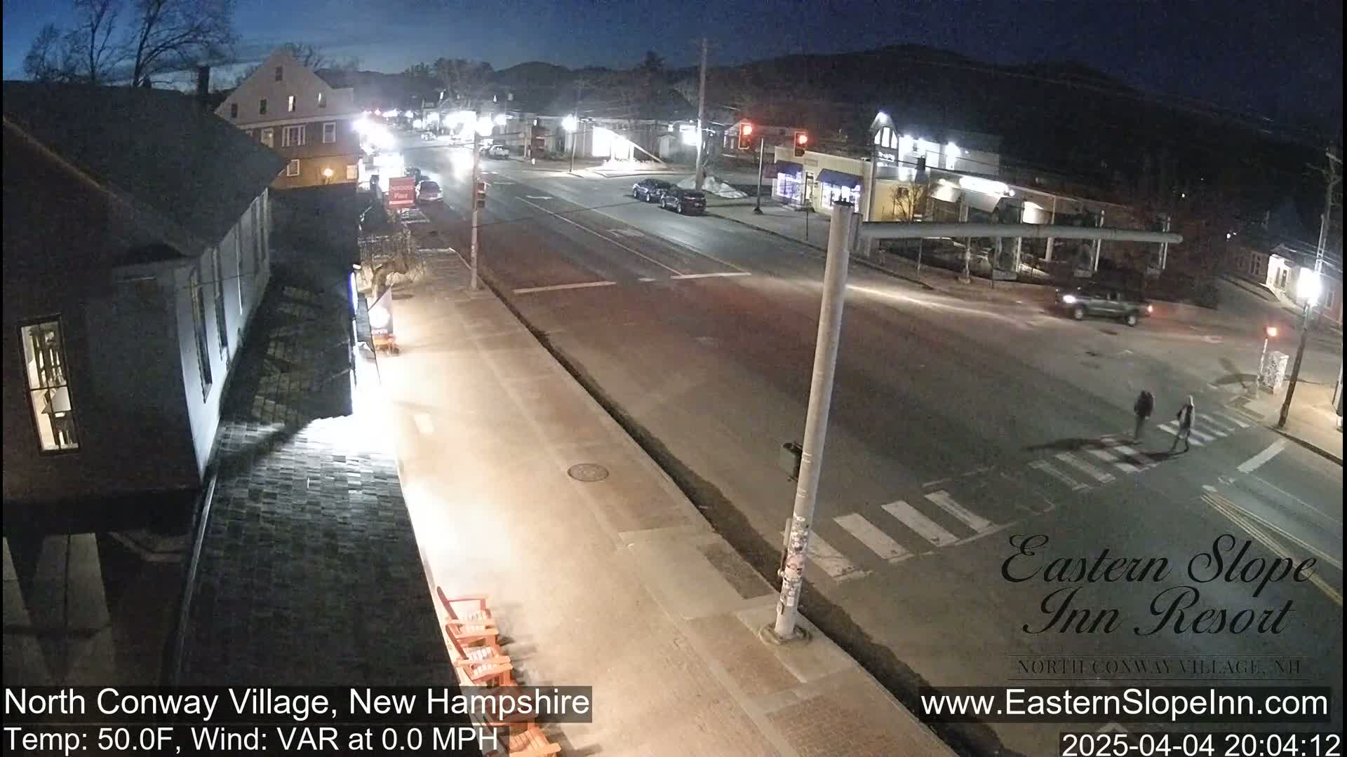 A nighttime street scene shows a mostly empty road with a few cars and pedestrians, under clear, cool conditions.