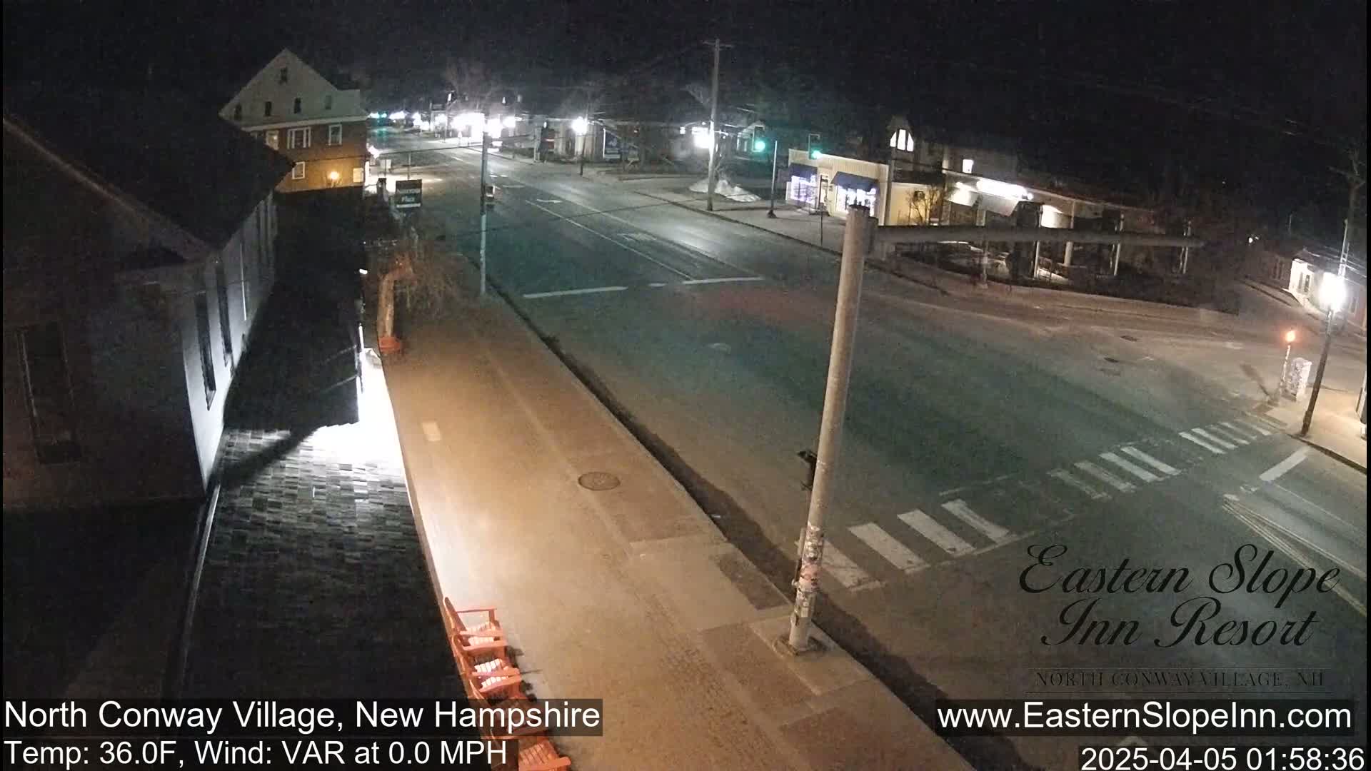 A nighttime view of a mostly empty street intersection in a small town, with a few buildings visible under clear skies and calm winds.