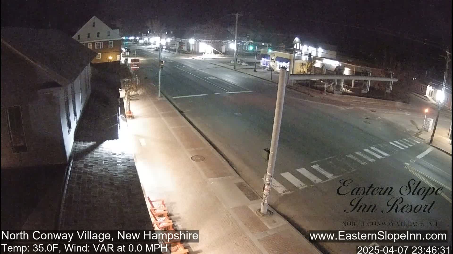 A nighttime, high-angle view of a mostly empty street intersection in a small town, with calm weather conditions.
