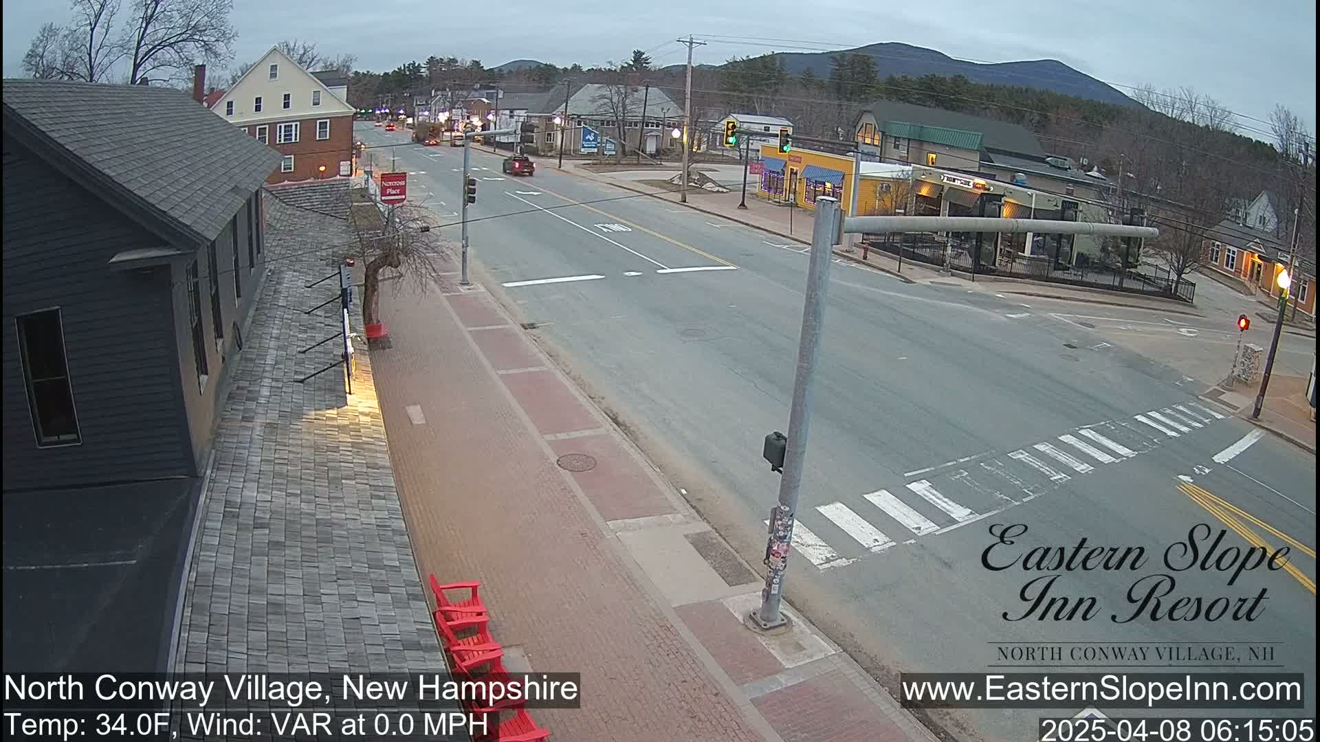 A mostly empty street scene in a small town, under an overcast sky, with a few buildings and cars visible.