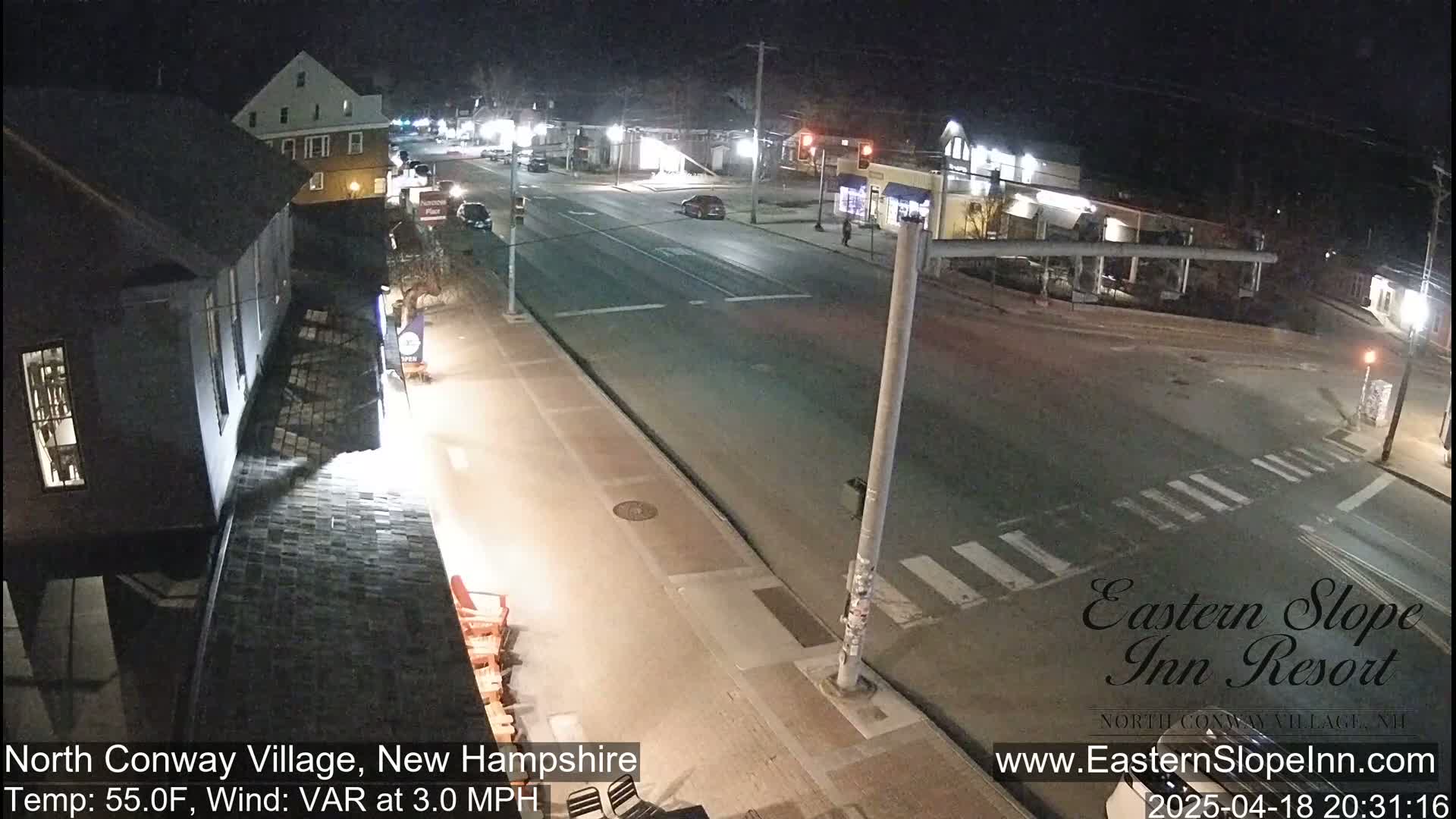 A nighttime street scene shows a mostly empty road intersection with a few cars and buildings under a clear sky, with a temperature of 55°F and a variable wind at 3.0 mph.