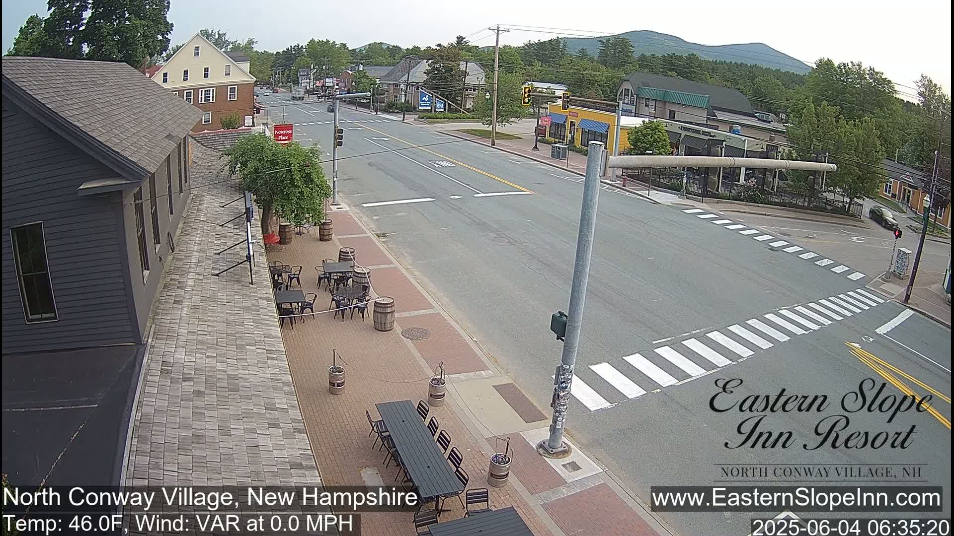 A mostly empty street scene in a village, with outdoor seating at a restaurant beside the road under a clear sky.
