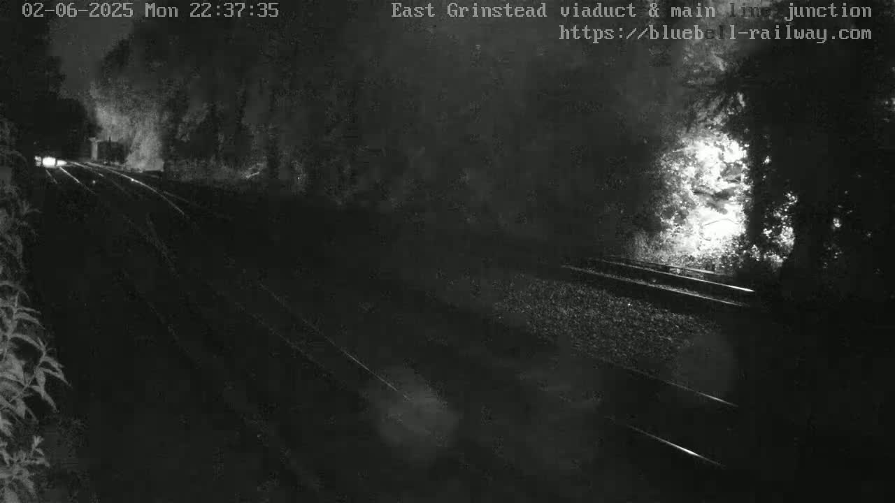 A nighttime, rainy view of train tracks extending into the darkness, partially illuminated by lights in the distance.