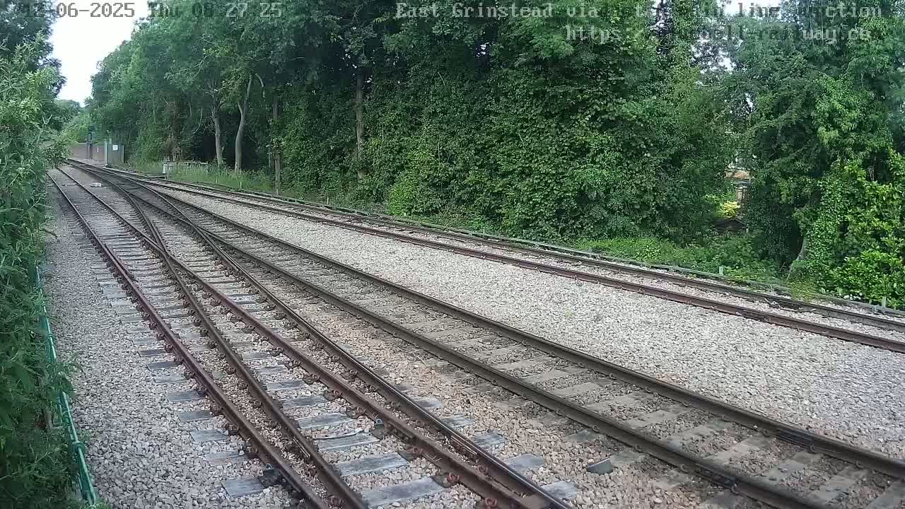 A view down a set of train tracks bordered by lush green vegetation on a sunny day.