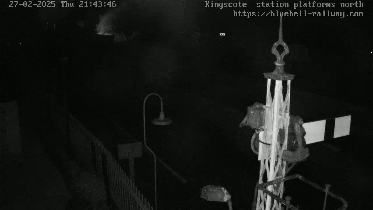 A nighttime, low-light view of a railway signal and a section of platform fencing.