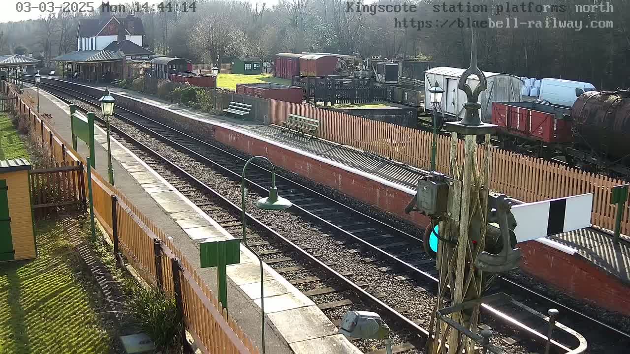 A sunny view of a train station platform with several railway cars and a station building visible.