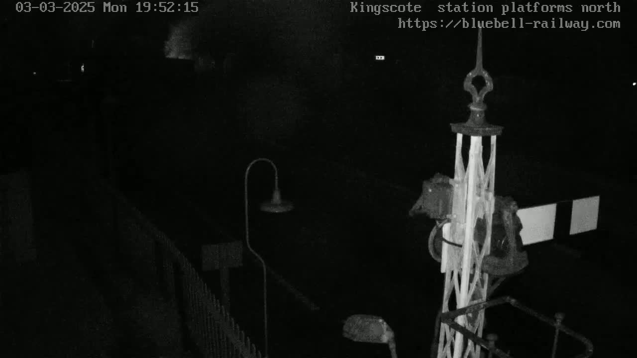 A nighttime, low-light view of a train platform with a signal and lamp visible.