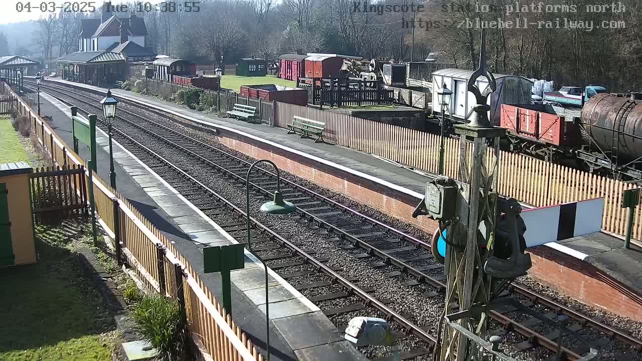 A sunny day at a train station with railway tracks,  platforms, and several freight cars parked nearby.