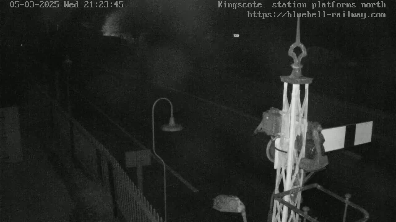 A nighttime, low-light image shows a railway platform with a signal and a lamppost.