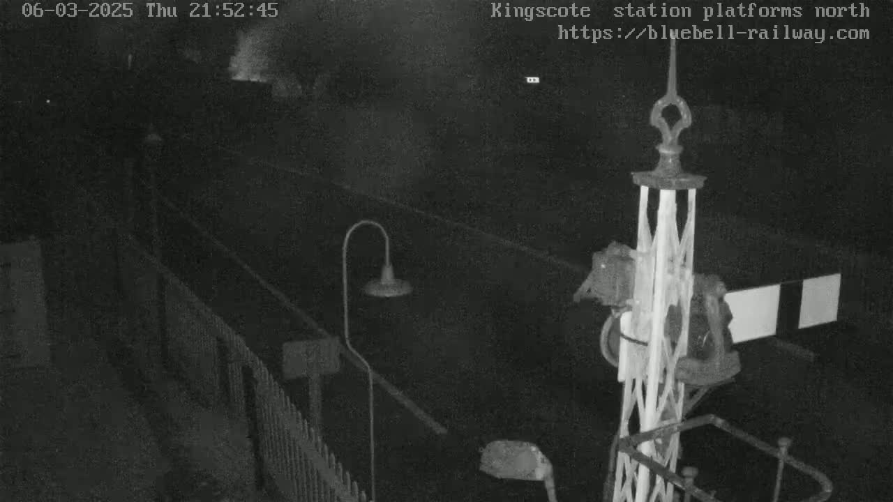 A nighttime, low-light view of a railway platform, showing a signal and a section of fencing.