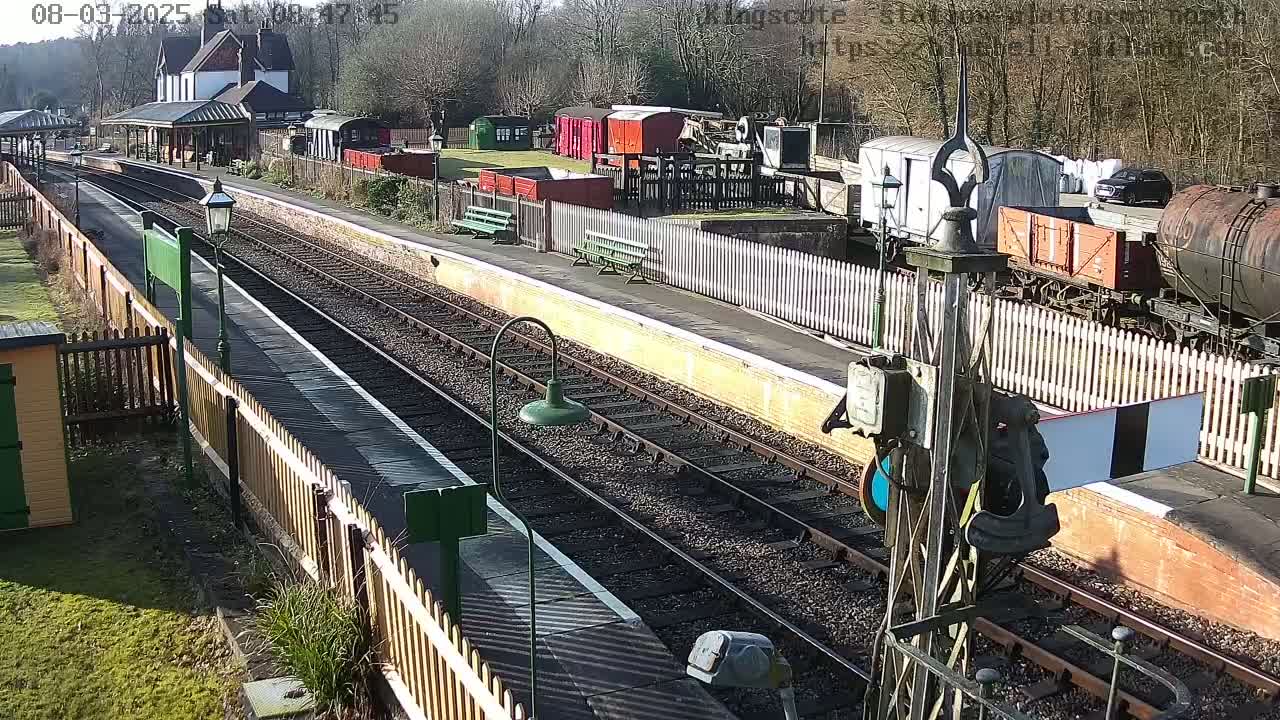 A sunny day at a train station with multiple railway tracks, various train cars, and a station building.