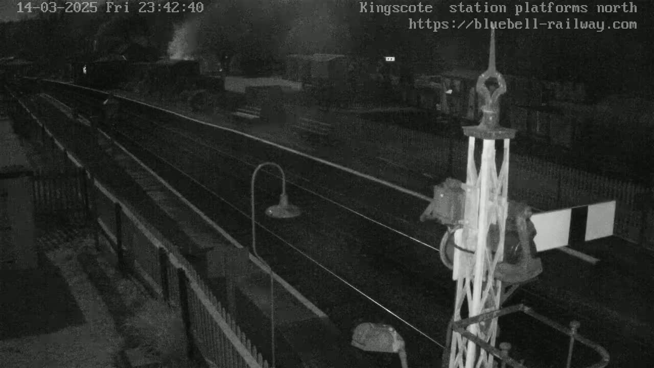 A nighttime, low-light view of a train on a track, passing by a railway signal, at what appears to be a station platform.