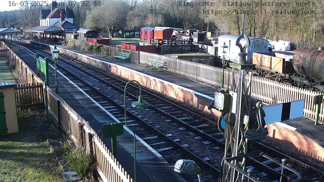 A sunny day at a train station with multiple train cars and a station building visible.