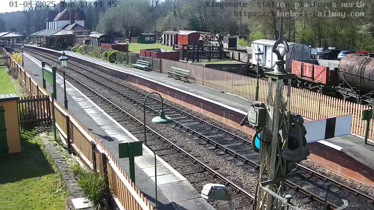 A sunny day at a train station with multiple railway tracks, several railway cars, and a station building.