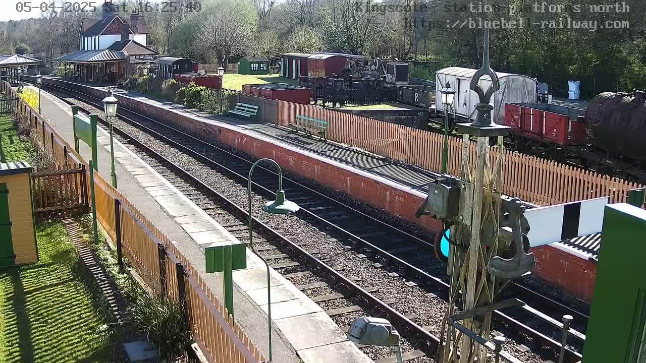 A sunny day at a train station shows multiple train cars, a station building, and train tracks extending into the distance.