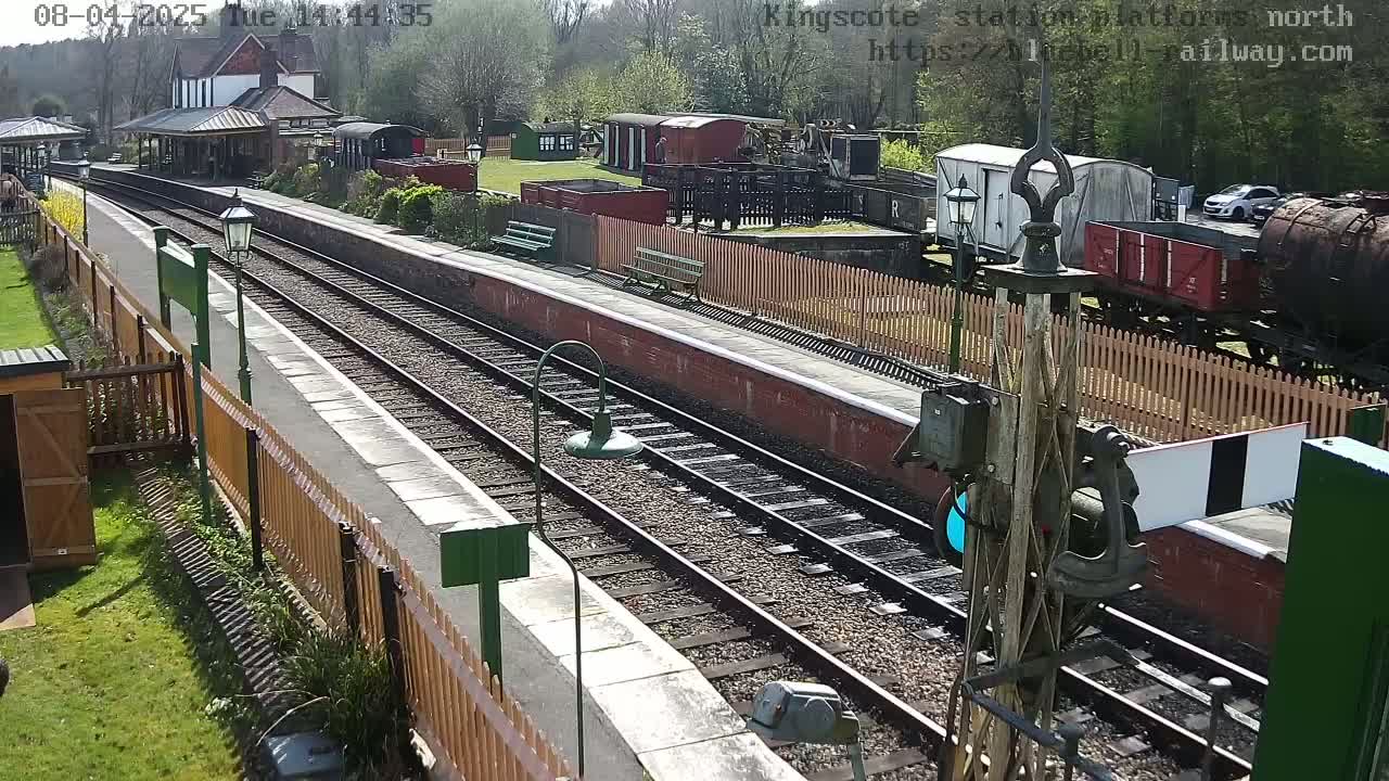 A sunny day at a train station with multiple train cars and tracks,  a platform, and wooden fences.