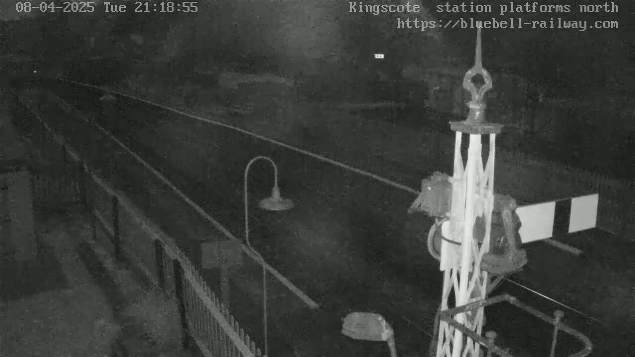 A nighttime low-light view of a railway platform with a signal and fences.