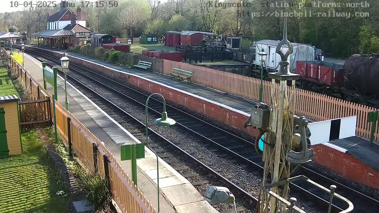 A sunny day at a train station with multiple railway tracks, several railcars, and a station building.