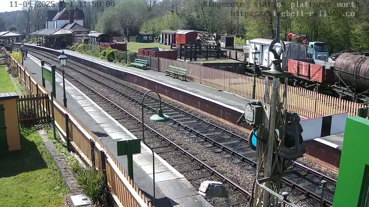 A sunny day at a train station shows railway tracks, platforms, several train cars, and a building.