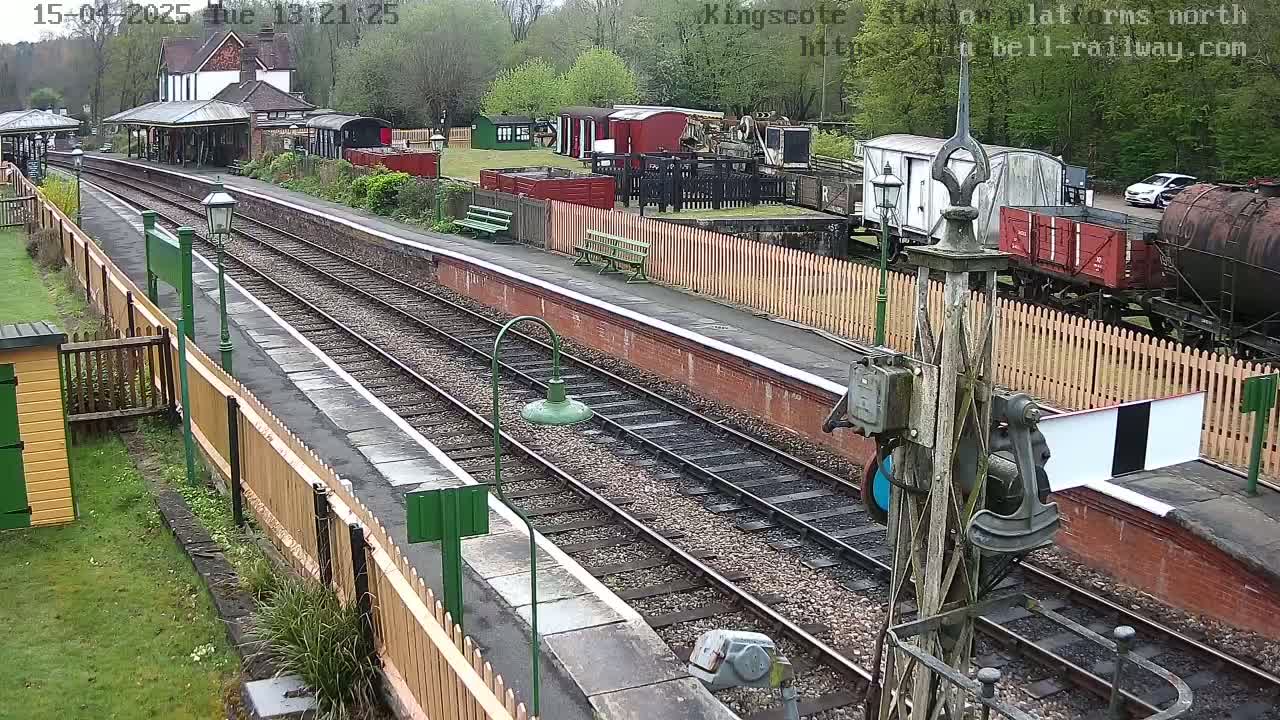 A train station platform with multiple train tracks, railway cars, and a small building under an overcast sky.