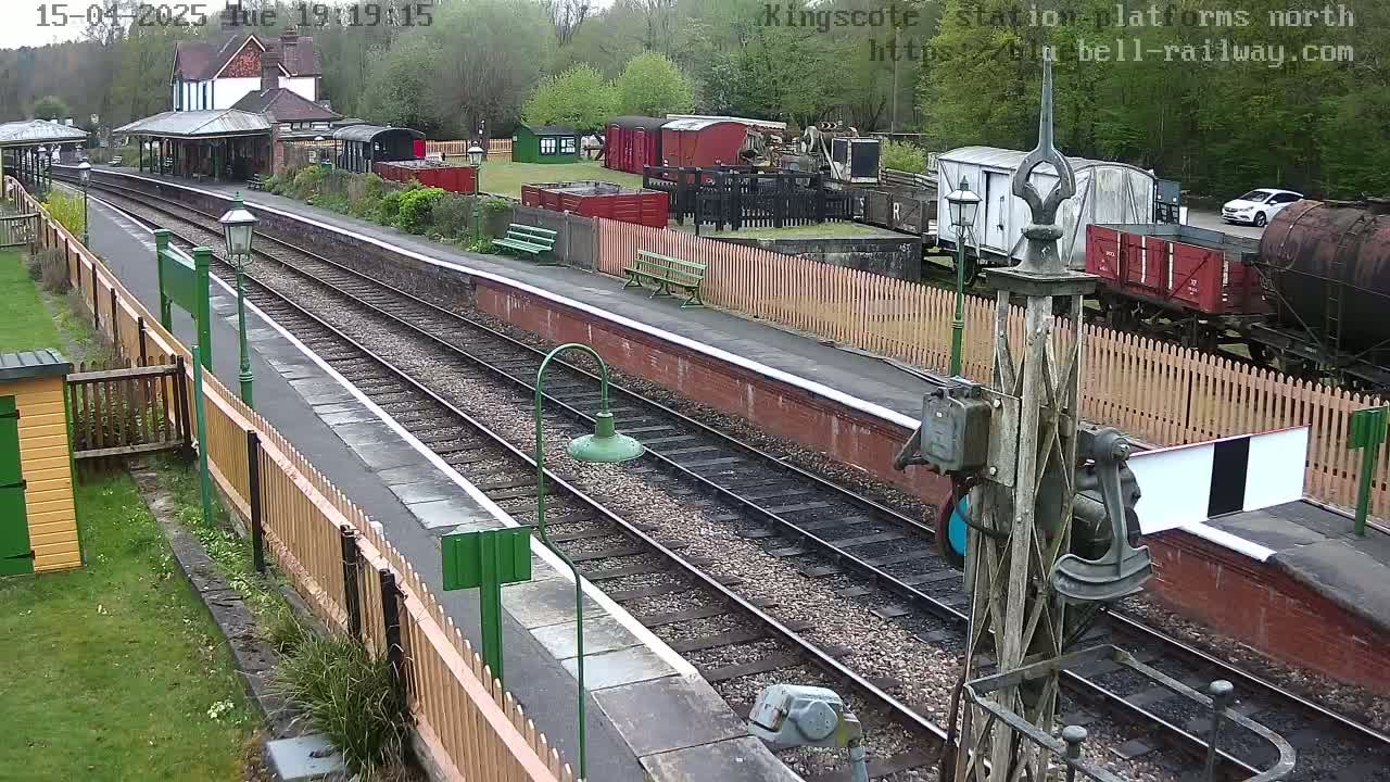 A high-angle view of a train station platform with multiple railway tracks, several railway cars, and a car parked in the distance under a cloudy sky.