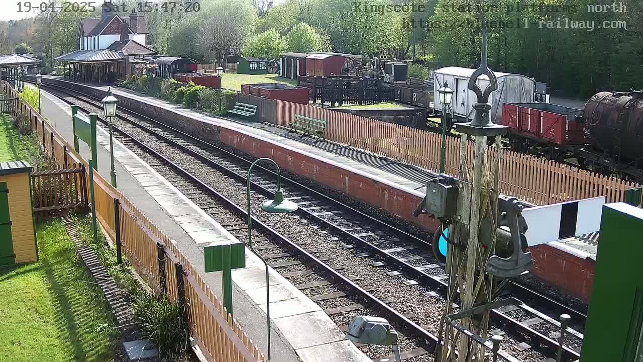 A sunny view of a train station platform with several railway carriages and a small building in the background.