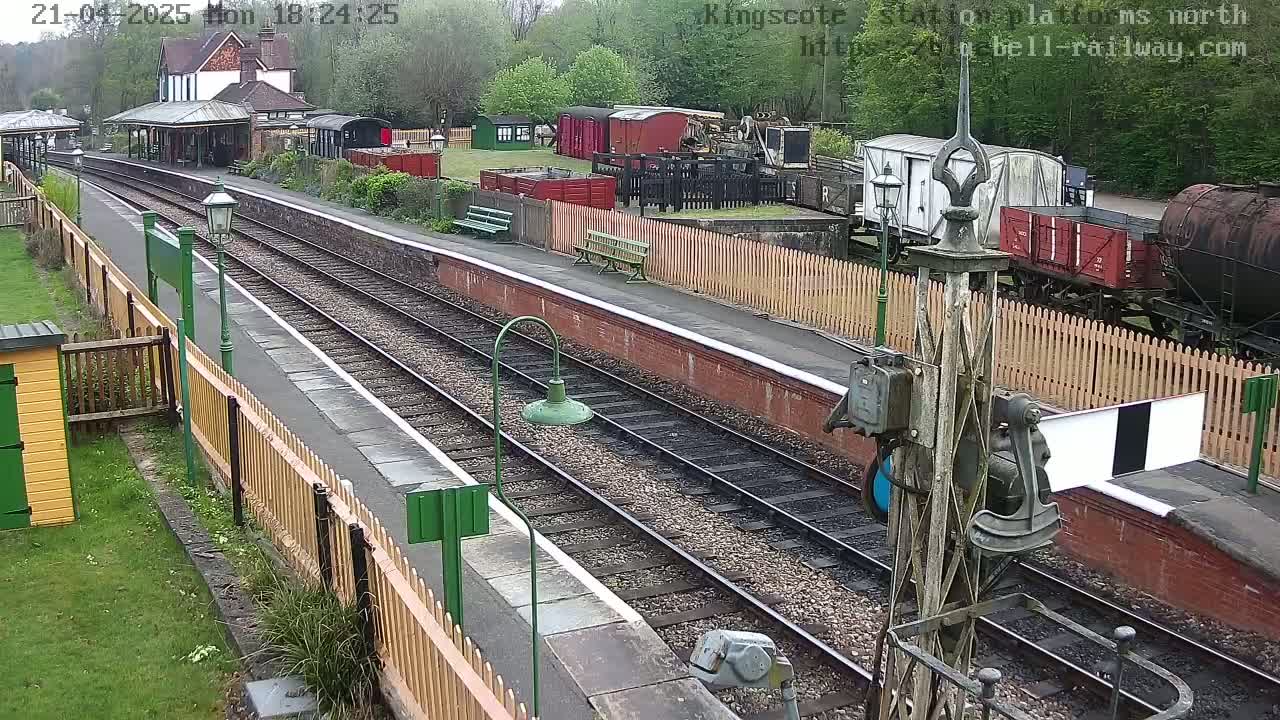 A train station platform with railway tracks, several railway cars, and a station building is seen on a cloudy day.