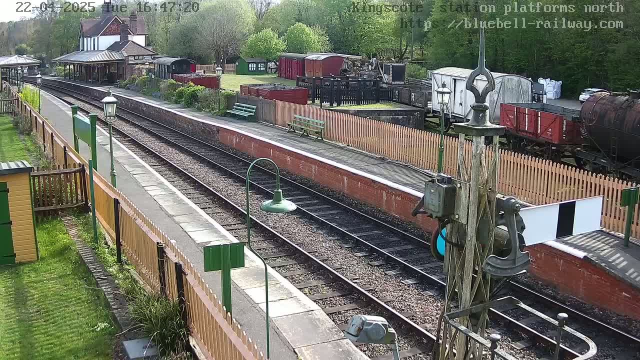 A sunny day at a train station with multiple railway tracks, several train cars, and a station building.