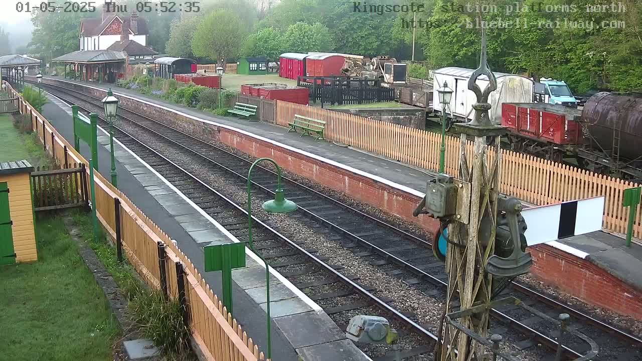 A train station platform with multiple train tracks, railway cars, and a small building, on an overcast day.