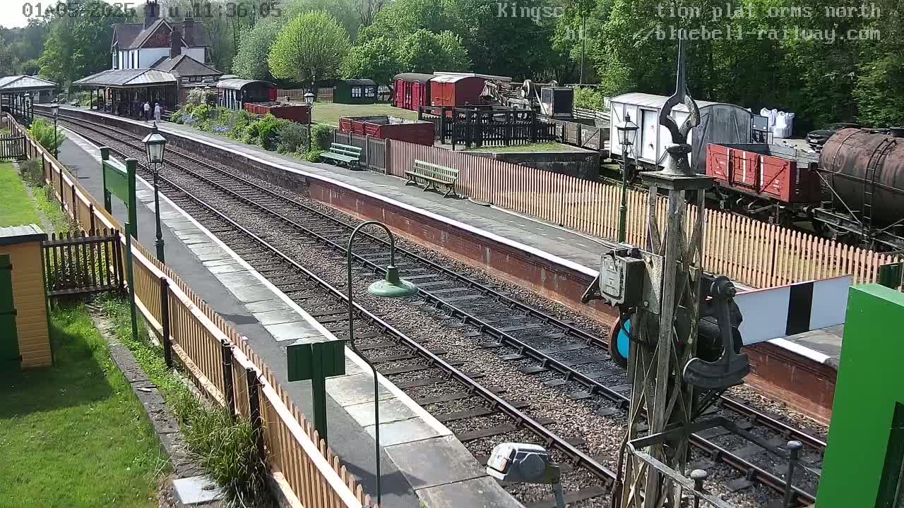 A sunny day at a train station with multiple train cars and a station building, showing a view down the railway tracks.