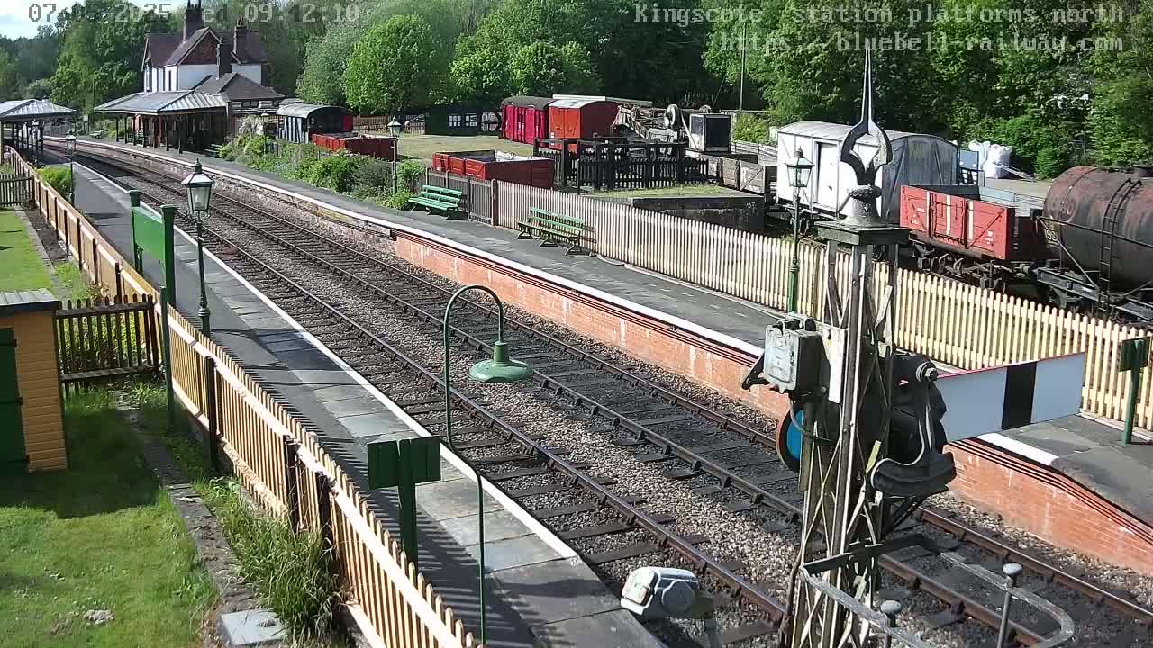 A sunny view of a train station platform with several railway cars and a station building in the background.