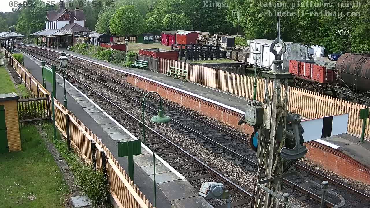 A railway station platform with several railcars and a building in the background on a partly sunny day.
