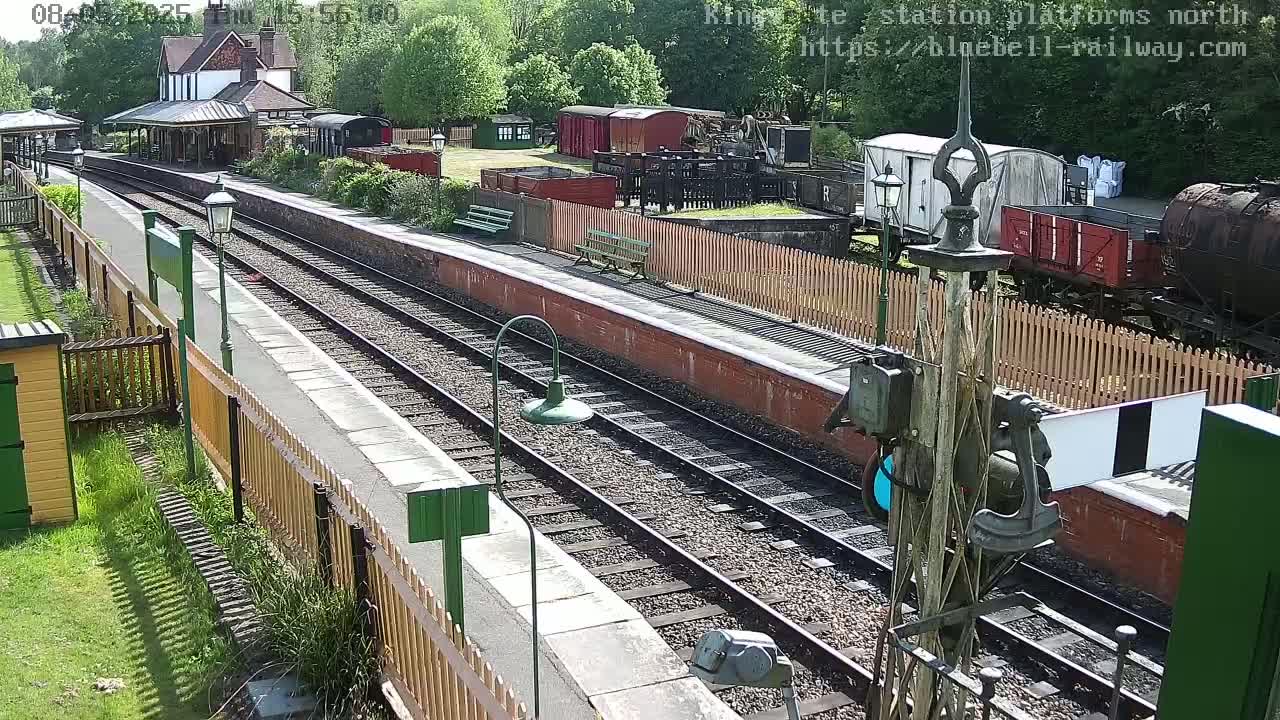 A sunny day at a train station platform with multiple train cars and a station building visible in the background.