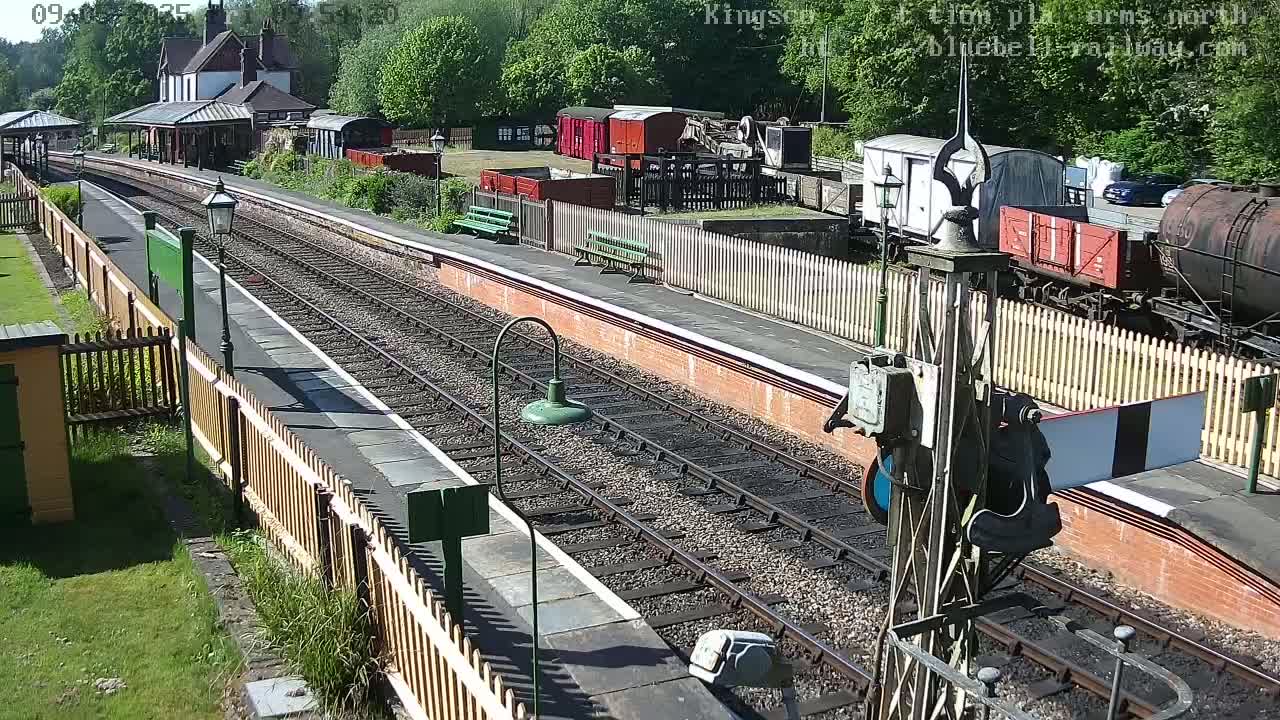 A sunny day at a train station with multiple railway tracks, several railway cars, and a station building.
