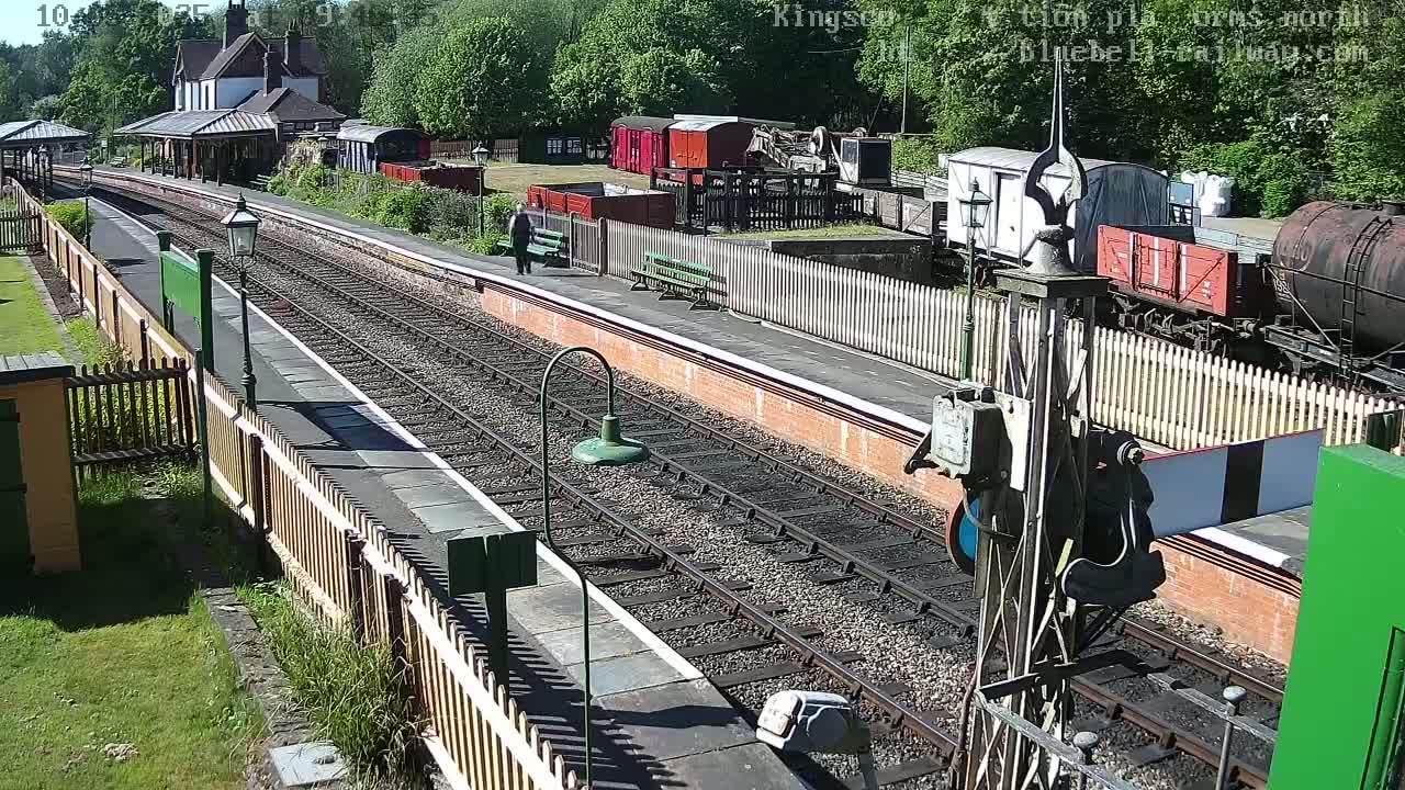 A sunny day at a train station with multiple railway cars, a station building, and a person walking on the platform.